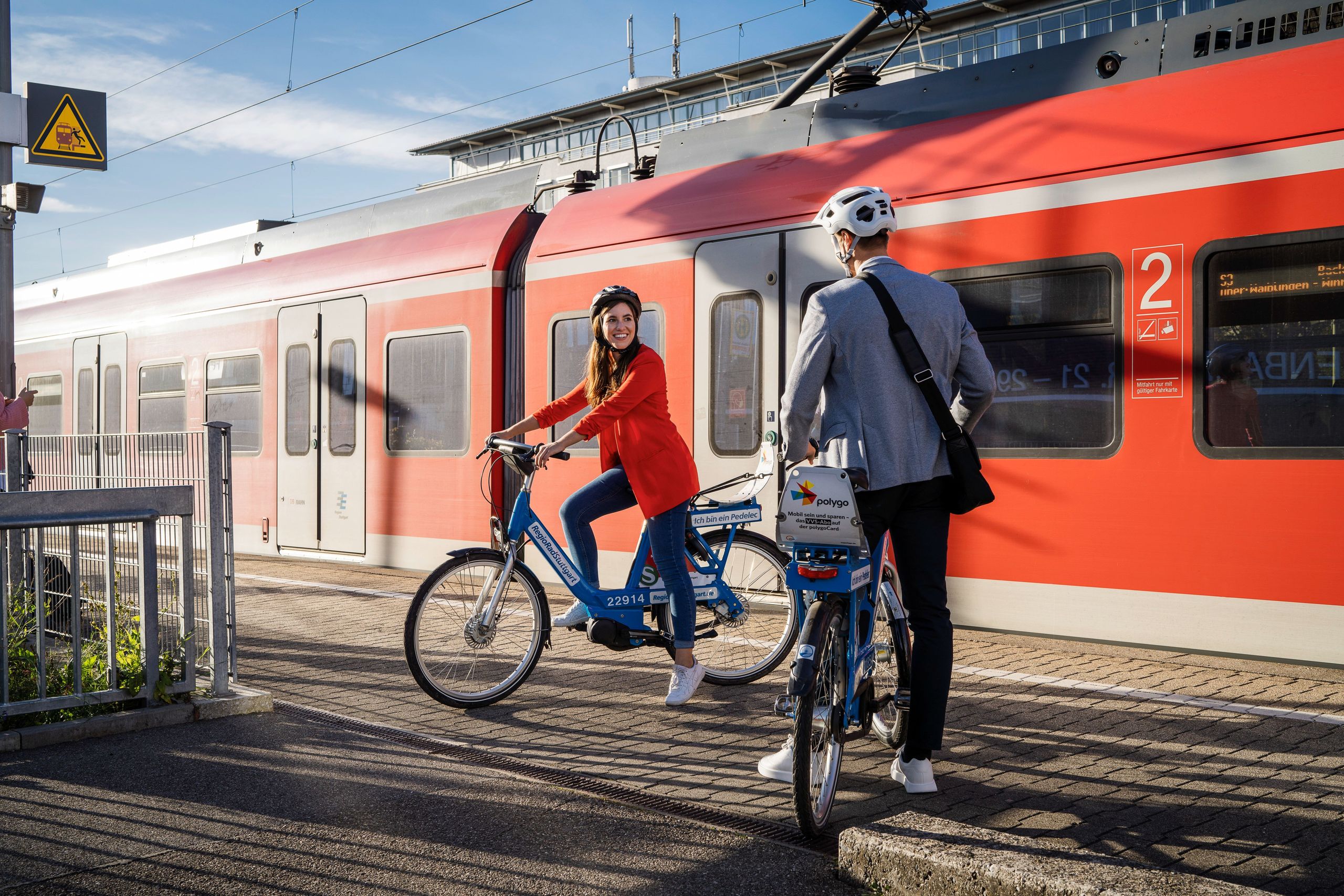 Woman and man standing with RegioRadStuttgart pedelecs on the railway track in front of a train
